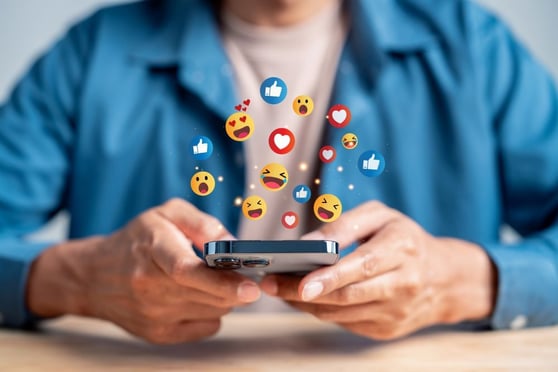 Person holding a phone, with emojis floating above the phone.