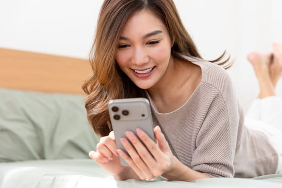 Happy young woman using smartphone for social media in bed