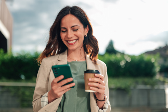 Smiling businesswoman checking smartphone on a coffee break outdoors