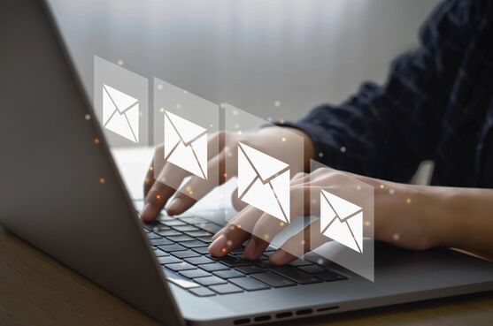 Person at a laptop, with email icons floating over the keyboard.