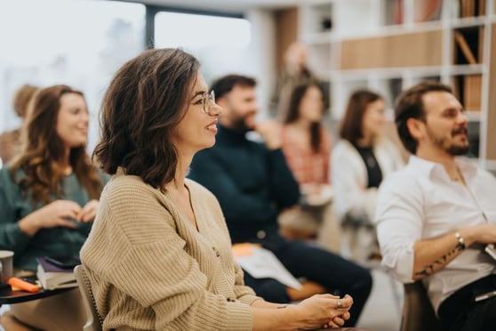 Smiling woman participating in a professional workshop with colleagues in a modern office setting, conveying engagement and teamwork.