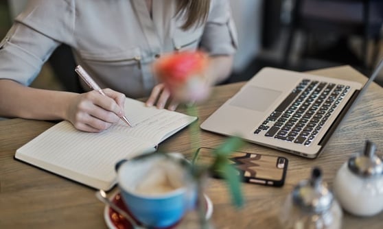 Person sitting at a desk, writing on a notepad