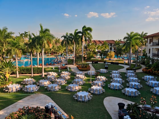 An aerial photograph of an outdoor event on a manicured green lawn within a tropical resort