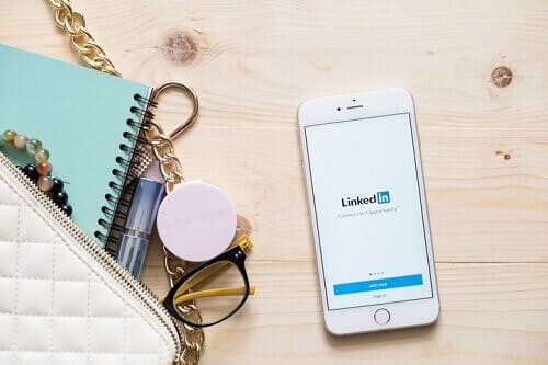Purse with scattered items on a wooden table, with an open cell phone next to it. It's showing the LinkedIn login screen.