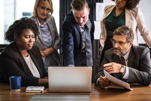 People sitting and standing around a laptop.