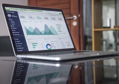 Open laptop on a glass table, showing analytics charts and graphs.