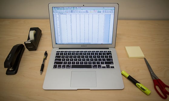 Image of an open laptop on a desk, with a spreadsheet on the screen.