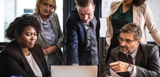 People sitting and standing around a laptop.