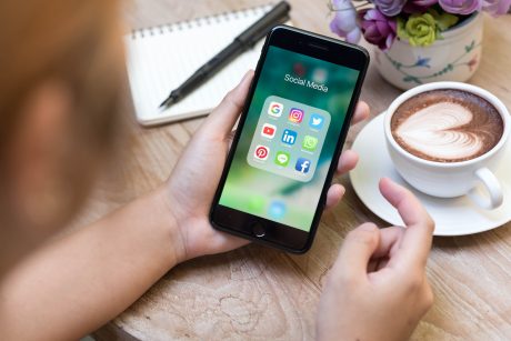 Person sitting at a table, holding a cell phone, with a cup of coffee in the background.