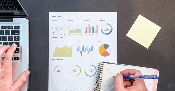 Person writing on a notepad, with an nanalytics report in the background.