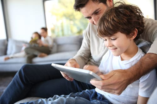 Man and child sitting at a couch, looking at a tablet together.