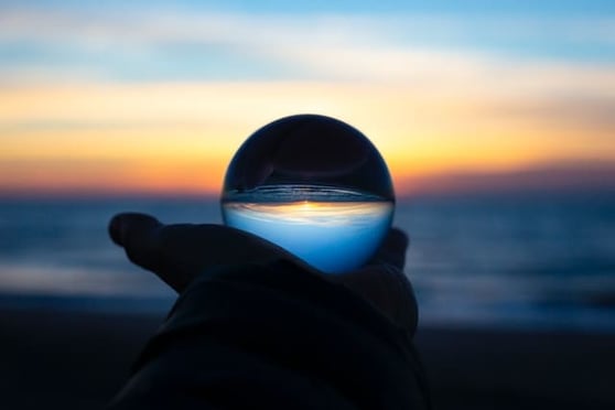 Person holding a crystal ball on a beach at sunrise