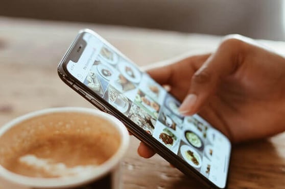 Person scrolling Instagram while sitting at a table drinking coffee.