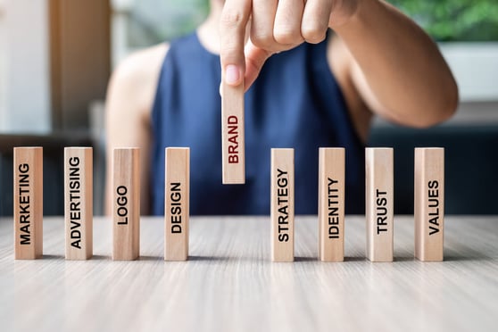 Businesswoman hand placing or pulling wooden Dominoes with BRAND text.