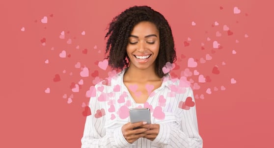 Woman browsign through social media on cellphone with hearts flying around, pink background