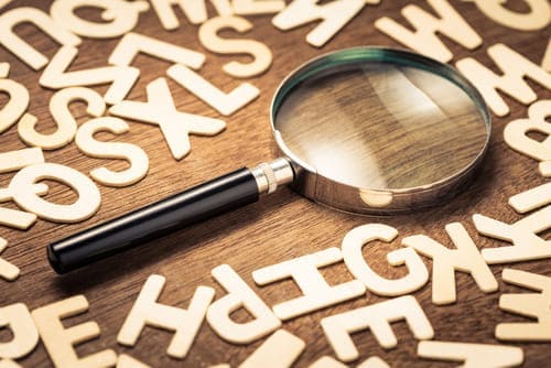 Magnifying glass with many wood letters of English alphabets.