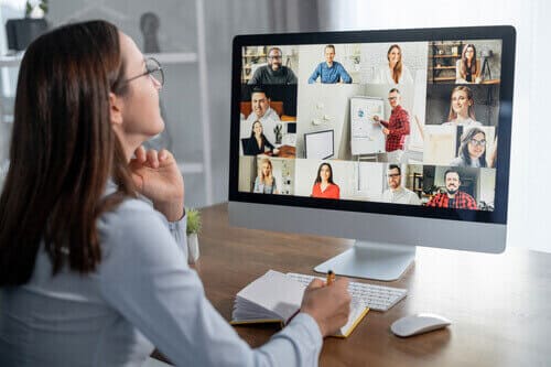 Woman looking at a computer screen filled with various people in a meeting.