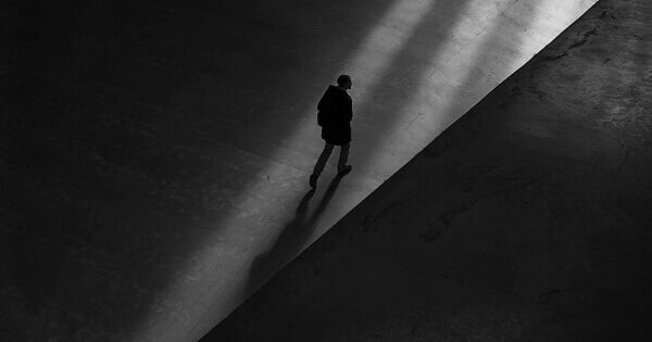 Person walking down a dark hallway, heading towards a stream of light.