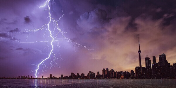 Toronto skyline by the water, with a dark and stormy sky. A ray of lightning is striking.